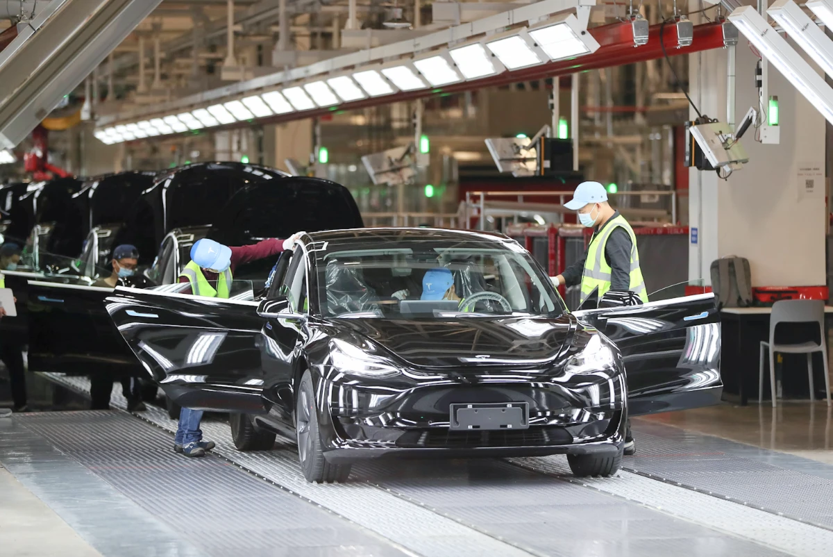 Tesla Model Y production line at the Shanghai Gigafactory with workers inspecting the vehicle